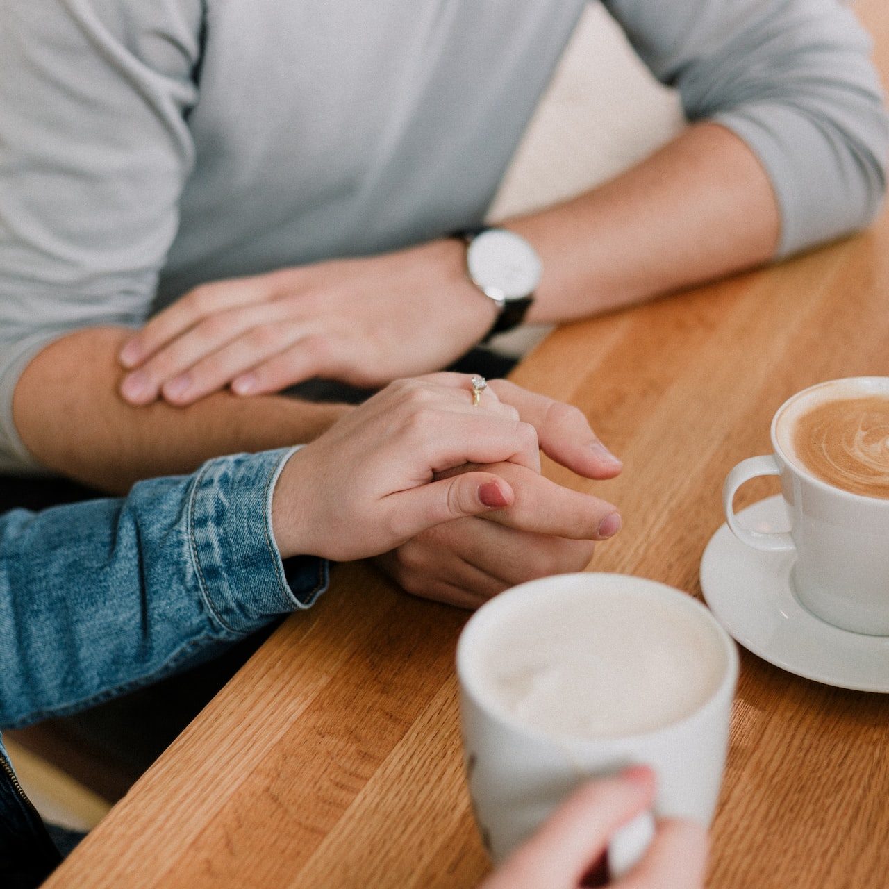 A couple reassuring each other while holding hands and drinking coffee.