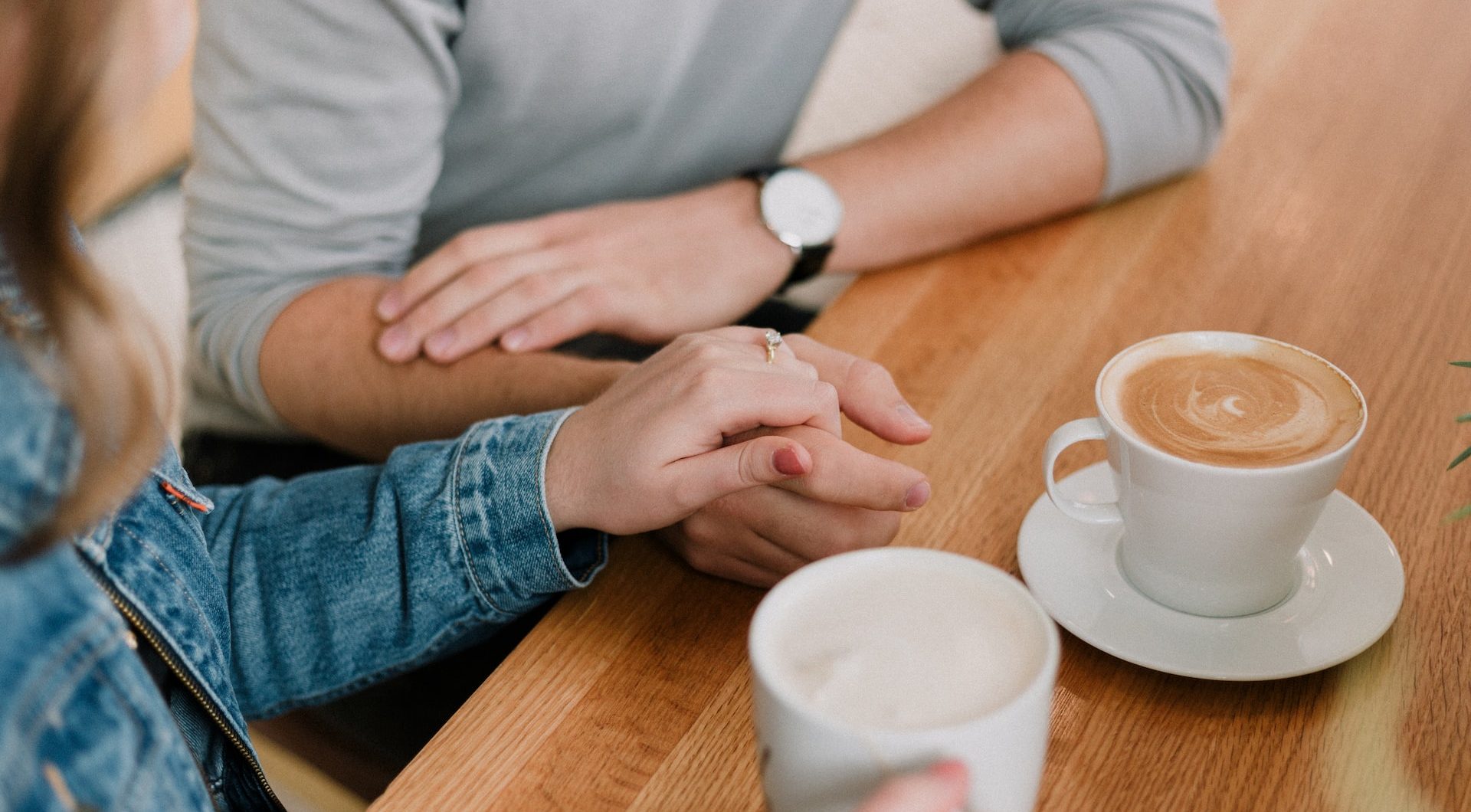 A couple reassuring each other while holding hands and drinking coffee.