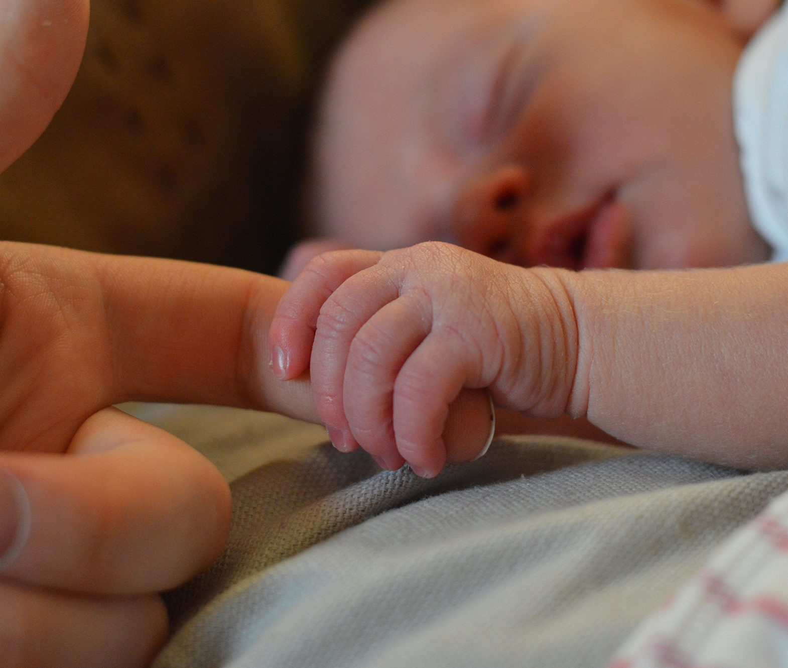A baby asleep holding an adults finger
