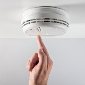 Finger pressing a ceiling smoke alarm test button