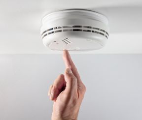 Finger pressing a ceiling smoke alarm test button
