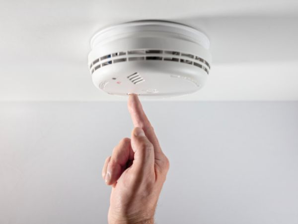 Finger pressing a ceiling smoke alarm test button