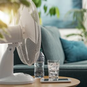 Electric fan and a glass of water on a table at home