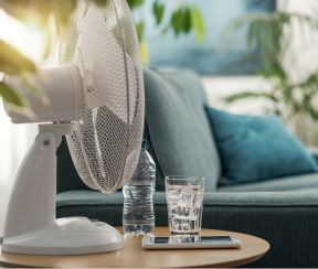 Electric fan and a glass of water on a table at home