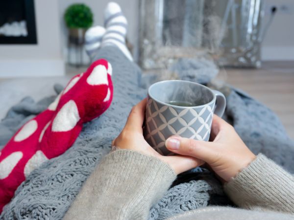 Person at home with a hot drink, thick socks and a hot water bottle