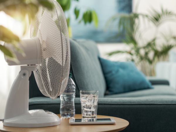 Electric fan and a glass of water on a table at home