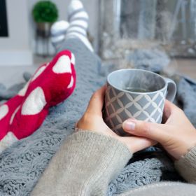 Person at home with a hot drink, thick socks and a hot water bottle