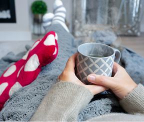 Person at home with a hot drink, thick socks and a hot water bottle